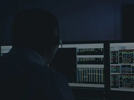 A race engineer uses ATLAS in a race team strategy room. Multiple screens show race telemetry and other information, and another screen shows a red race car is shown on track.